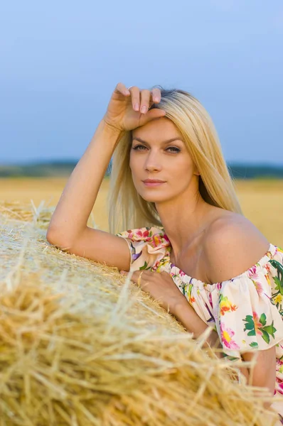 一位身穿五颜六色衣服 光着肩膀的美丽的欧洲女人站在田野和天空背景下的草堆旁 — 图库照片