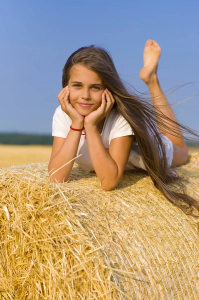 可爱的光着脚的长发姑娘躺在蓝天的草堆上 — 图库照片