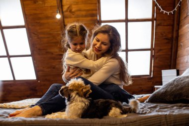 Anne ve kızı evcil köpekleriyle çatı katındaki yatak odasında oynamaktan memnunlar.