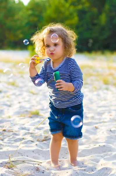 Vtipné Kudrnaté Dítě Učí Foukat Mýdlové Bubliny Písečné Pláži Pozadí — Stock fotografie