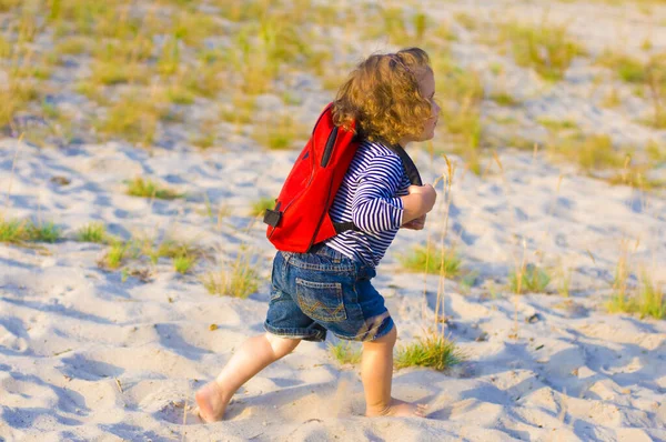Красивая Кудрявая Малышка Ходит Босиком Песку Красным Рюкзаком Спине — стоковое фото