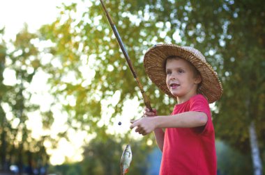 Bir elinde olta, diğer elinde balık tutan yedi yaşında bir çocuk var.