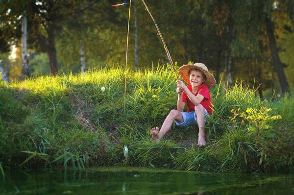 cheerful barefoot boy sitting near the lake and fishing