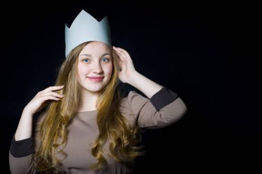 Kafasında karton bir taç olan güzel sarışın kameraya tatlı tatlı bakıp gülümsüyor.