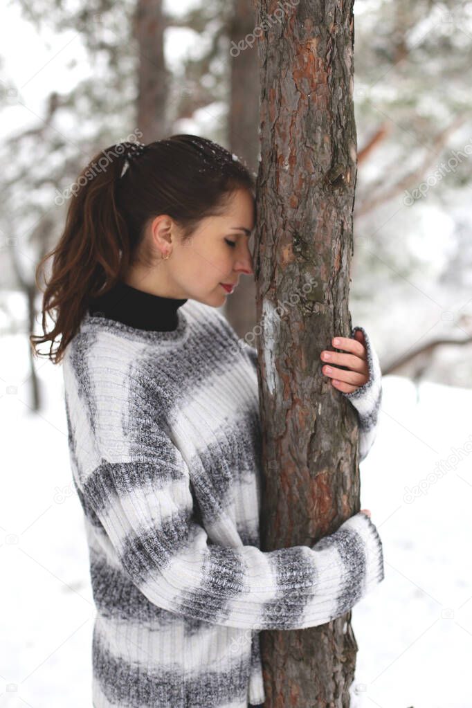young dark-haired european woman stands in a winter forest hugging a tree
