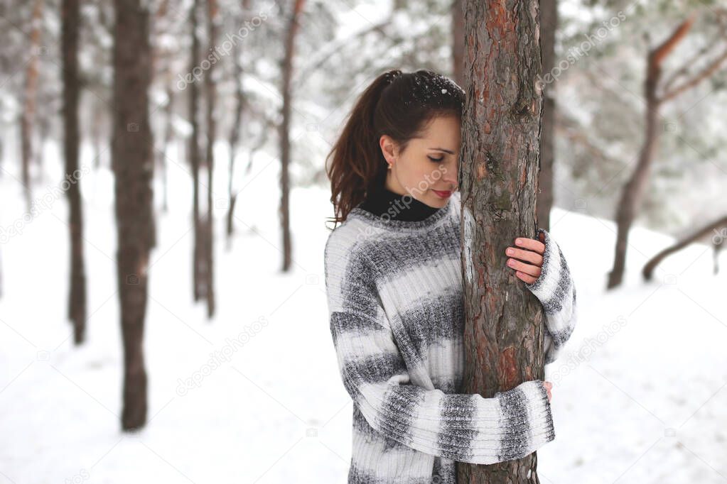 pretty dark-haired european woman stands in a winter forest hugging a tree