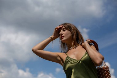 İnce ipek elbiseli genç esmer elleri alnında, sokakta kafa karıştırıcı bir şekilde dikiliyor.