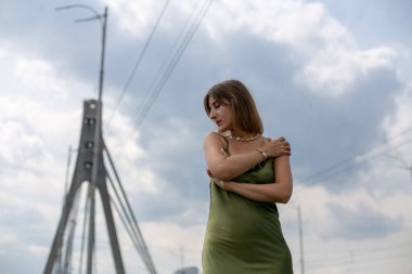 İpek elbiseli, ince, güzel bir esmer köprüde dalgın dalgın duruyor ve kollarıyla kendine sarılıyor.