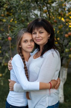Güzel anne ve genç kızı bir elma bahçesinin ortasında birbirlerine sarılıyorlar.