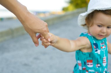 Komik bir kız çocuğu, mavi elbiseli ve beyaz panama şapkalı. Annesinin elinden tutup yaz parkına götürüyor.