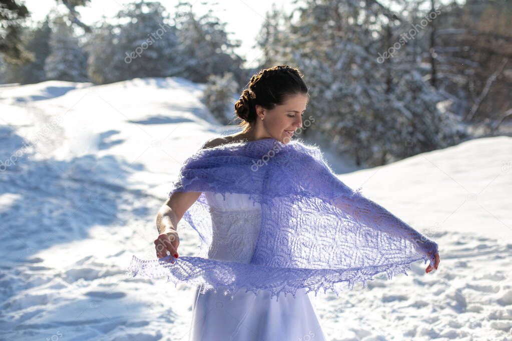 cute pretty dark-haired girl in a long white dress and a light purple knitted shawl joyfully whirls in the clearing of the winter forest