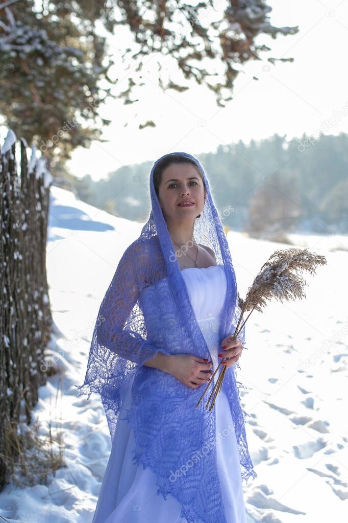 nice girl in a long white dress stands covered with a light purple openwork shawl against the background of a winter landscape