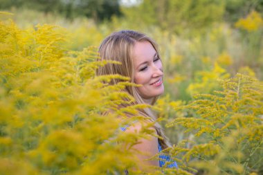 Güzel gülümseyen sarışın çiçek açan tarla bitkileriyle çevrili.