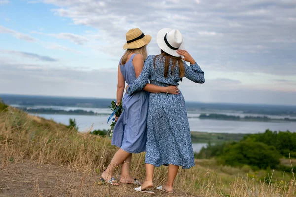 Две Молодые Длинноволосые Женщины Голубых Летних Платьях Шляпах Стоят Обнимаясь — стоковое фото