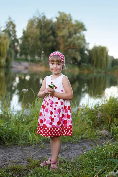 穿着红色粉红圆点的白色夏装的漂亮女孩站在河岸上 面对着美丽的夏季自然 — 图库照片
