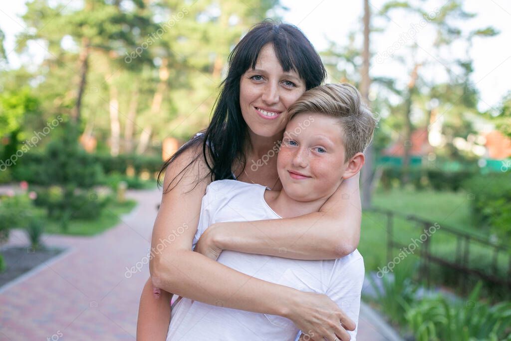 young long-haired brunette woman hugs from behind her teenager son for a walk in the park