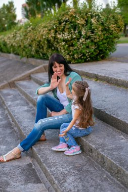 Genç anne ve üç yaşındaki kız günlük giysiler içinde yaz parkında birlikte eğleniyorlar.