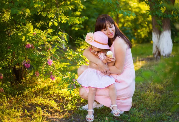 快乐的三十五岁的黑发姑娘拥抱着她心爱的小女儿 她的背景是美丽的夏季绿色和开花的植物 — 图库照片