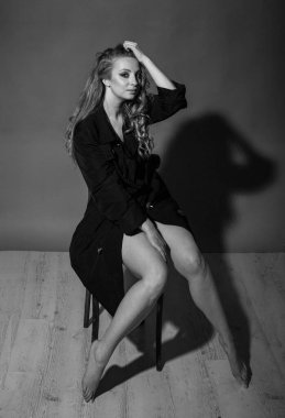 Güzel vücutlu çekici bir sarışın siyah pelerinli bir stüdyoda oturur ve dikkatlice uzaklığa bakar.