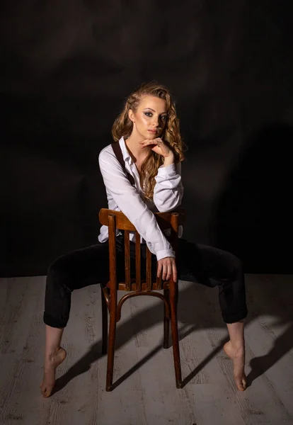 年轻美丽的金发女人穿着白衬衫 穿着黑色内裤 坐在工作室的椅子上 沉思地看着摄像机 — 图库照片