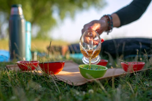 Siyah bluzlu kadın taze havadaki kaselere yeşil çay döker.