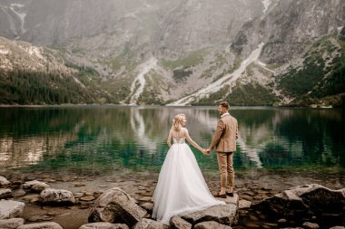 Polonya 'nın güneyindeki Tatra Dağları' ndaki Morskie Oko gölünde poz veren romantik gelin ve damat çifti.