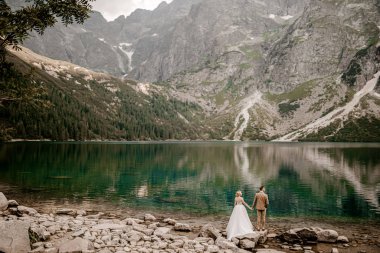 Polonya 'nın güneyindeki Tatra Dağları' ndaki Morskie Oko gölünde poz veren romantik gelin ve damat çifti.