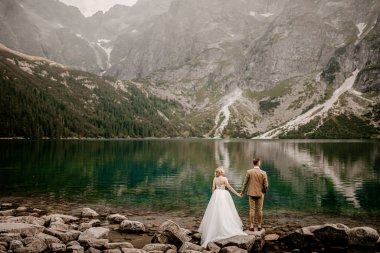 Polonya 'nın güneyindeki Tatra Dağları' ndaki Morskie Oko gölünde poz veren romantik gelin ve damat çifti.