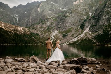 Genç gelin ve damat Polonya 'nın güneyindeki Tatra Dağları' nda Morskie Oko gölünde poz veriyorlar.