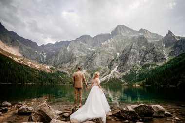 Genç gelin ve damat Polonya 'nın güneyindeki Tatra Dağları' nda Morskie Oko gölünde poz veriyorlar.