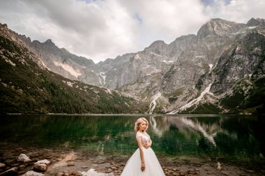 Polonya 'nın güneyindeki Tatra Dağları' nda Morskie Oko gölünde poz veren uzun beyaz elbiseli güzel gelin.