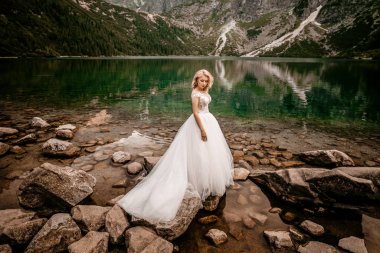 Polonya 'nın güneyindeki Tatra Dağları' nda Morskie Oko gölünde poz veren uzun beyaz elbiseli güzel gelin.