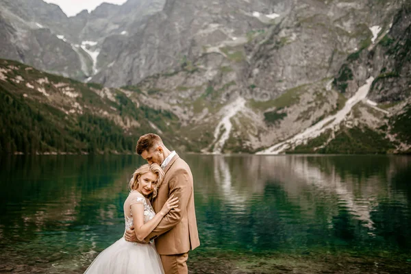 ポーランド南部のタトラ山脈のモルスキー オコ湖にポーズをとるロマンチックな若い花嫁と新郎のカップル — ストック写真