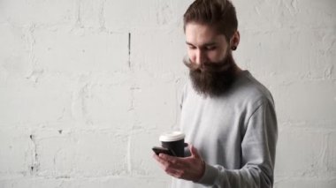 Genç adam kahve içiyor, cep telefonuna bakıyor. Mutlu sakallı adam gülümsüyor