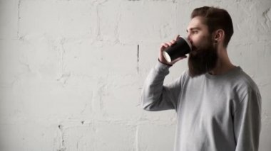 Genç sakallı adam pencereden dışarı bakarak kahve içer. Mola sırasında mutlu programcı