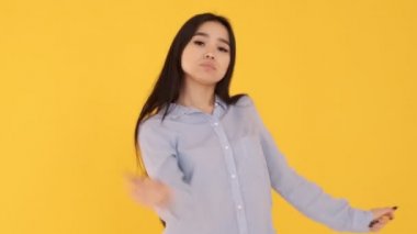 Sarı arka planda mavi gömlekli genç kız dans ediyor, gülümsüyor. Yavaş çekim