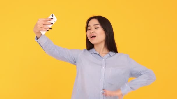 Una joven sobre un fondo amarillo hace una selfie. Hamming y payasadas . — Vídeos de Stock