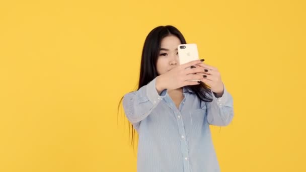 Girl makes selfie Asian woman on yellow background admiring them through phone — Stock Video