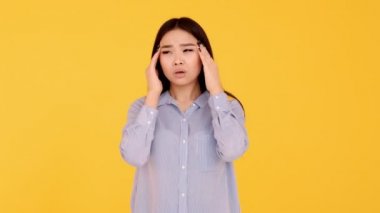 Sarı arka planda Asyalı genç bir kız. Kadınlarda baş ağrısı kavramı