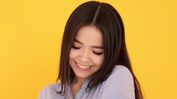 年轻的亚洲女孩在一个黄色的背景害羞。女人笑着和她调情 — 图库视频影像