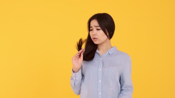 Une jeune fille regarde les cheveux des femmes asiatiques cheveux fendus sur un fond jaune — Video