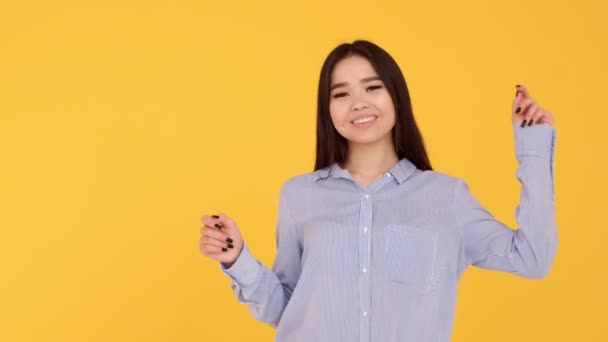 Una joven asiática está bailando y sonriendo sobre un fondo amarillo — Vídeo de stock