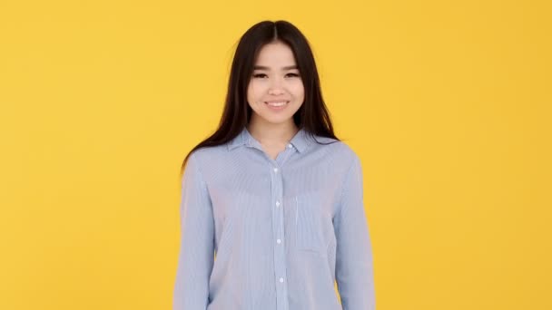 Young girl Asian on yellow background smiling and looking at camera — ストック動画