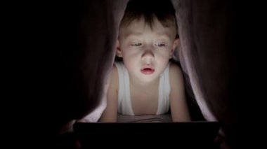 Küçük çocuk battaniyenin altında yatarken tabletle oynuyor. Saklanan çizgi filmleri izliyordum.