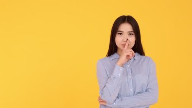 Sarı arka plandaki kız sessizliğin jestini gösteriyor