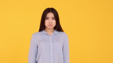 Asyalı mutsuz genç bir kız, bir hoşlanmama hareketi gösteriyor. Sarı arka plandaki kadın