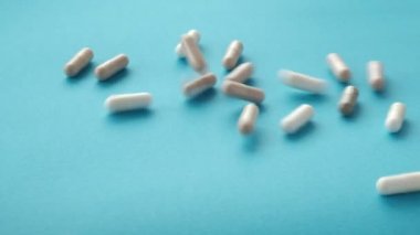 Beslenme takviyesi hapları mavi arka planda yavaş çekim video tabletlerine düşüyor