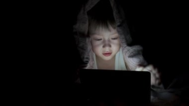 Küçük çocuk battaniyenin altında yatarken tabletle oynuyor. Saklanan çizgi filmleri izliyordum.