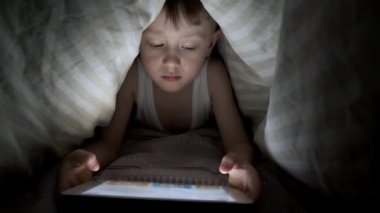 Küçük çocuk battaniyenin altında yatarken tabletle oynuyor. Saklanan çizgi filmleri izliyordum.