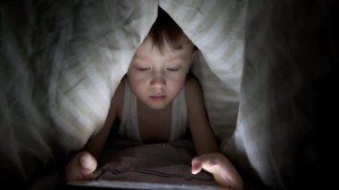 Küçük çocuk battaniyenin altında yatarken tabletle oynuyor. Saklanan çizgi filmleri izliyordum.